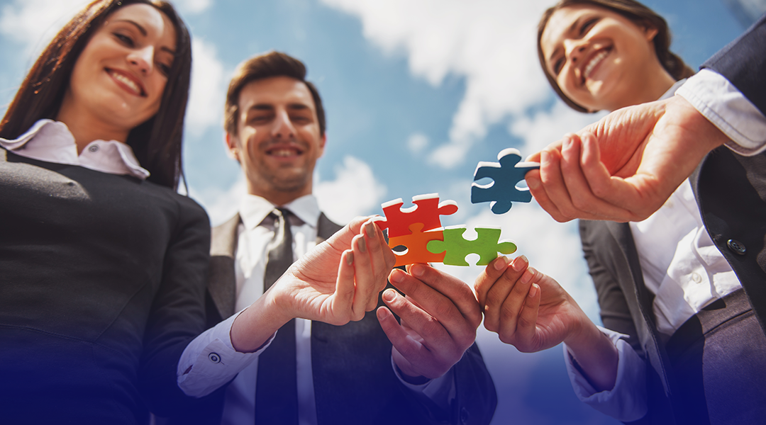 Business professionals in suits join colorful puzzle pieces, symbolizing teamwork and collaboration outdoors.